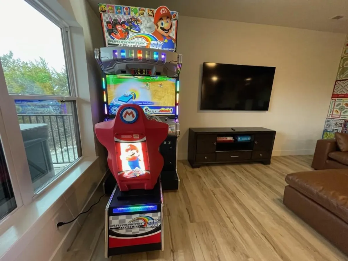 A vibrant interior scene featuring a Mario arcade machine, television, and a brown leather couch. The space is designed for fun, with entertainment options for both gaming and relaxation, suggesting an ideal spot for game nights or movie marathons.