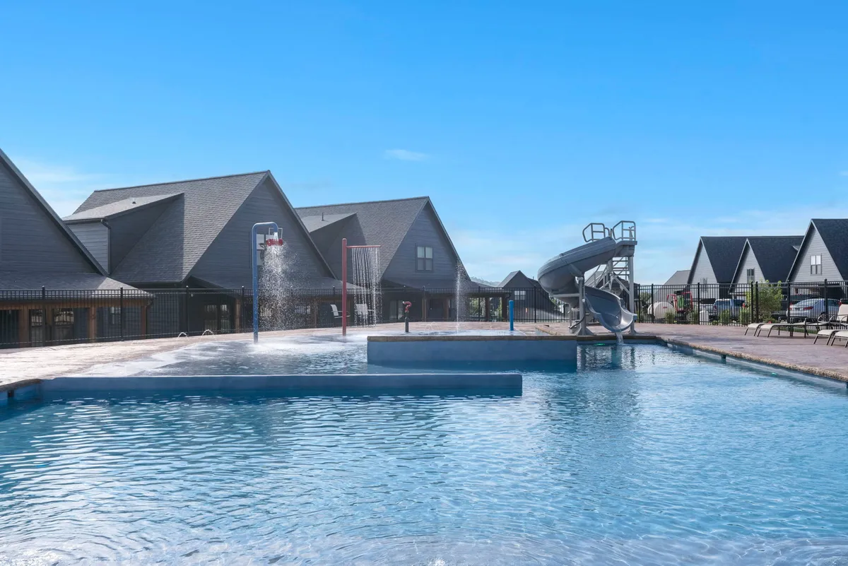 This vibrant exterior image showcases a sparkling swimming pool with a water slide, surrounded by comfortable lounge chairs and nearby buildings. The scene is lively, with hints of families and children enjoying playful water activities and group gatherings.