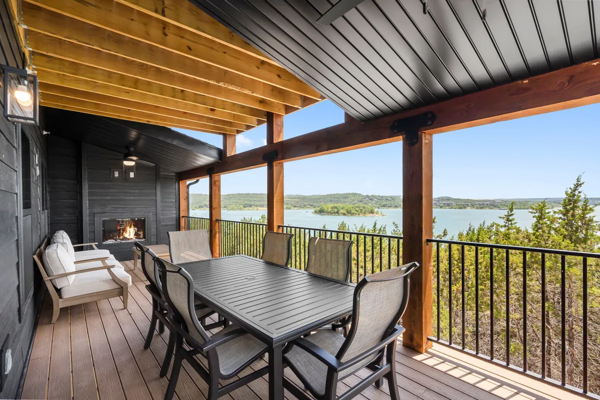 A serene exterior shot of an outdoor dining table adjacent to a cozy fireplace, with a stunning view of the lake in the background. The table is set for al fresco meals and the fireplace creates a warm, inviting atmosphere for evening gatherings.
